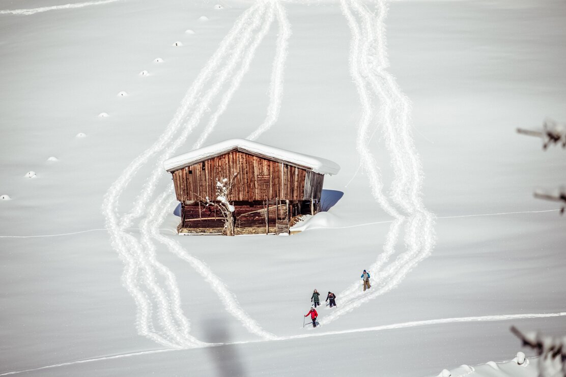 Auf diesem Bild zu sehen sind vier Personen, welche gerade eine Schneeschuhtour durch die wundervolle Schneelandschaft in Alpbach machen, des Weiteren zu sehen ist eine alte Tenne  | © Alpbachtal Tourismus | shootandstyle 