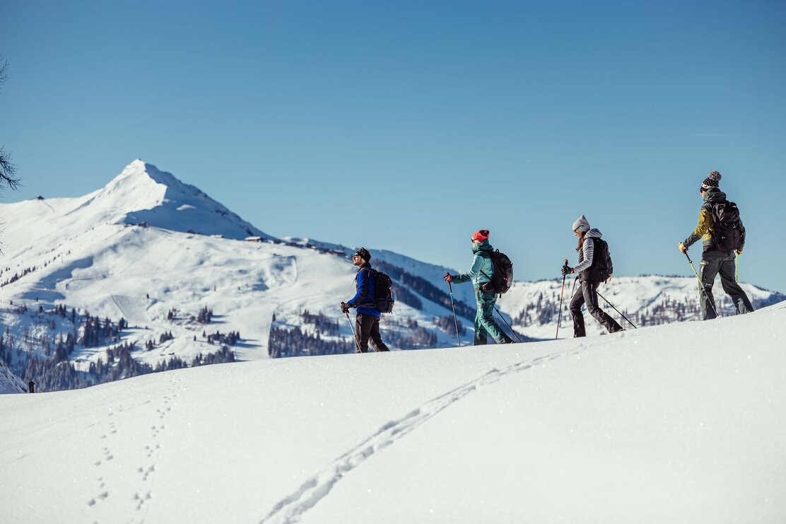 Eine Vierköpfige Freundesgruppe macht eine Schneeschuhwanderung durch Alpbach, rundherum die weiße Winterlandschaft  | © Alpbachtal Tourismus | shootandstyle 