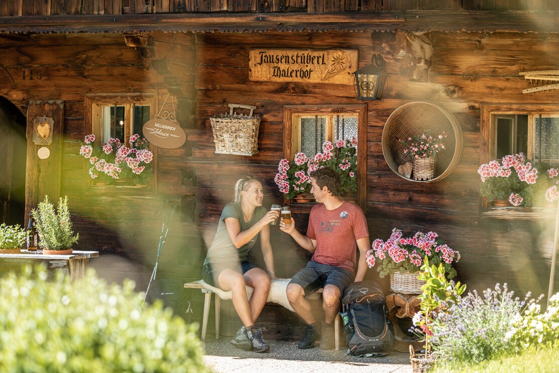 Ein paar gießt gerade ihr Bier im Garten der Jausenstation Thalerhof, im Garten blühen viele Blumen und Sträucher  | © Alpbachtal Tourismus | shootandstyle 