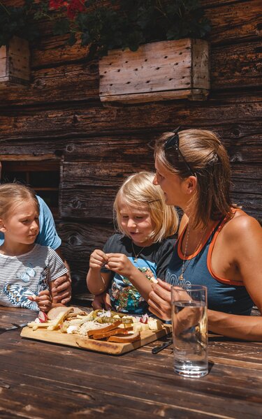 Eine Familie isst genüsslich eine Brettljause auf der Farmkehralm in Inneralpbach | © Alpbachtal Tourismus | Mathäus Gartner 