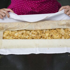 Eine Frau rollt den befüllten Apfelstrudel zu einer Strudelform ein | © Tirol Werbung 