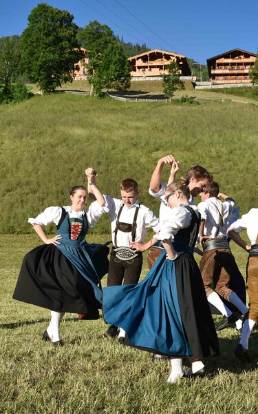 Die traditionelle Tanzgruppe Alpbacher Plattler, beim tanzen auf einer Wiese, im Hintergrund ein paar Häuser  | © Alpbacher Plattler