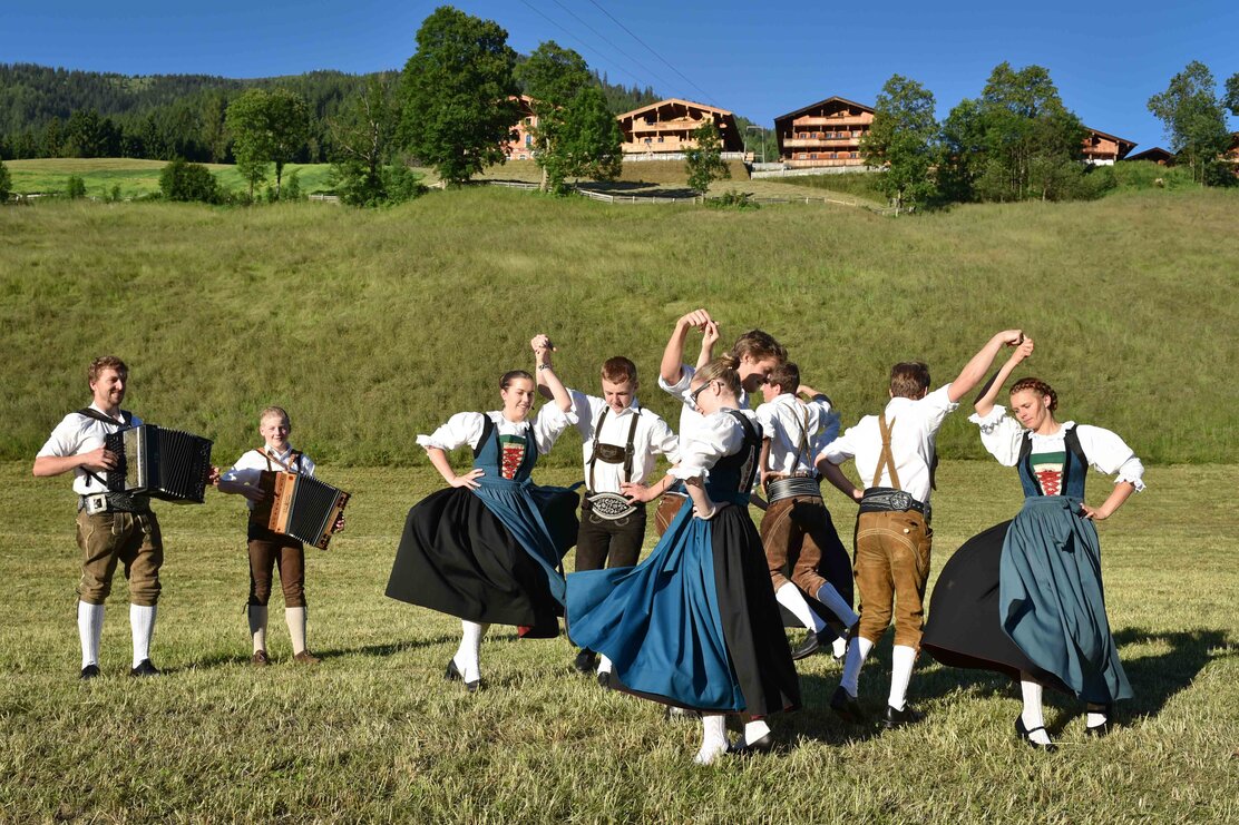 Die traditionelle Tanzgruppe Alpbacher Plattler, beim tanzen auf einer Wiese, im Hintergrund ein paar Häuser  | © Alpbacher Plattler