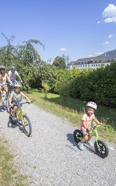 Eine vierköpfige Familie macht gemeinsam eine Radtour am Inn entlang, mit Blick auf das damalige Kloster in Rattenberg | © Alpbachtal Tourismus | Matthias Sedlak 