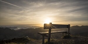 Eine Bank im Vordergrund, im Hintergrund Sonnenaufgang mit Blick auf die Wiedersbergerhornbahn | © Alpbachtal Tourismus | shootandstyle