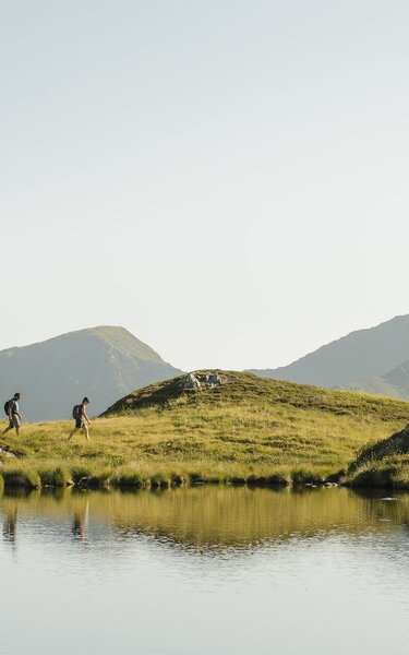 Ein Paar wandert entlang eines Sees, in Richtung des Gipfels Torkopf | © Alpbachtal Tourismus | E. Holzknecht 