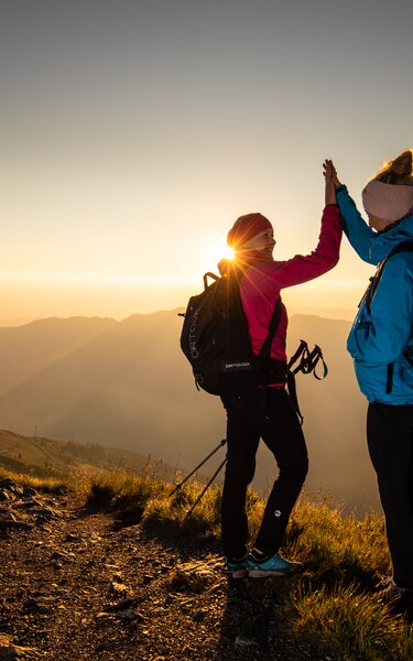 Zwei Freundinnen klatschen vor Freude in die Hände und genießen den Sonnenaufgang am Berg | © Alpbachtal Tourismus | shootandstyle 