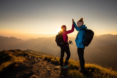 Zwei Freundinnen klatschen vor Freude in die Hände und genießen den Sonnenaufgang am Berg | © Alpbachtal Tourismus | shootandstyle 