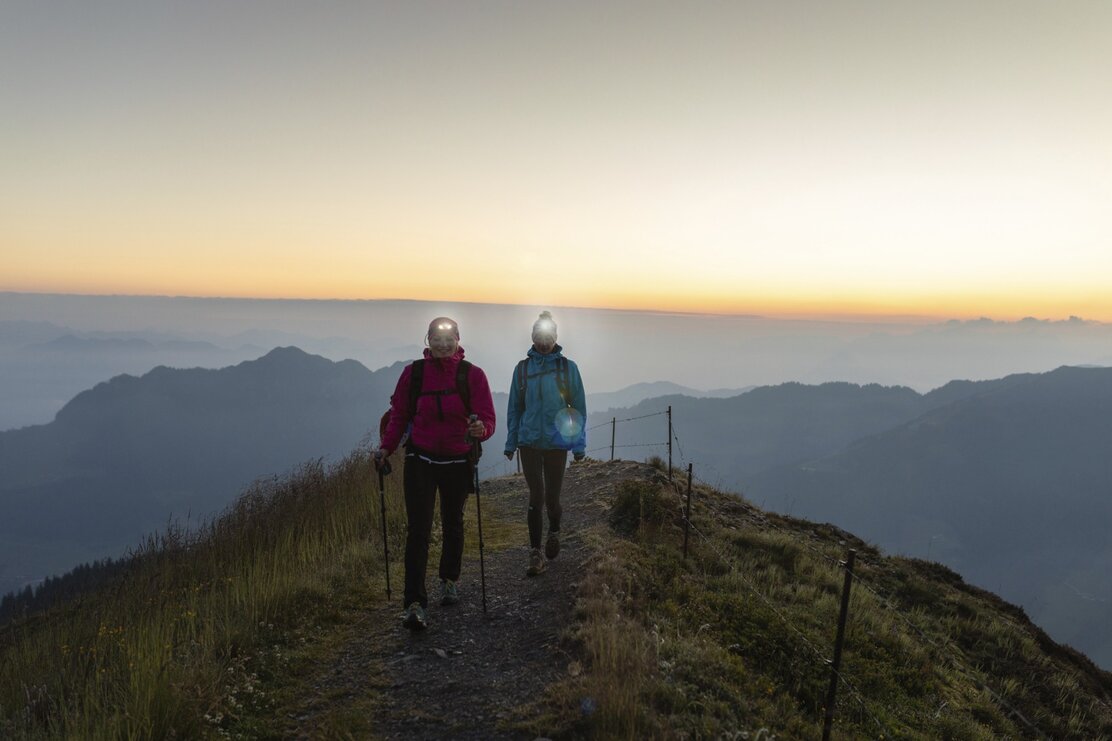 Zwei Freundinnen wandern entlang des Wiedersberger Horns, um den Gipfel zum Sonnenaufgang rechtzeitig zu erreichen, im Hintergrund verfärbt sich der Himmel schon in schönen Farben | © Alpbachtal Tourismus | shootandstyle 