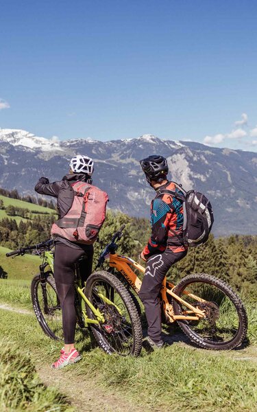 Ein Paar steht mit ihren E-Bikes auf einer Forststraße und genießen die Aussicht auf die leicht weißen Gipfel  | © Alpbachtal Tourismus | shootandstyle 